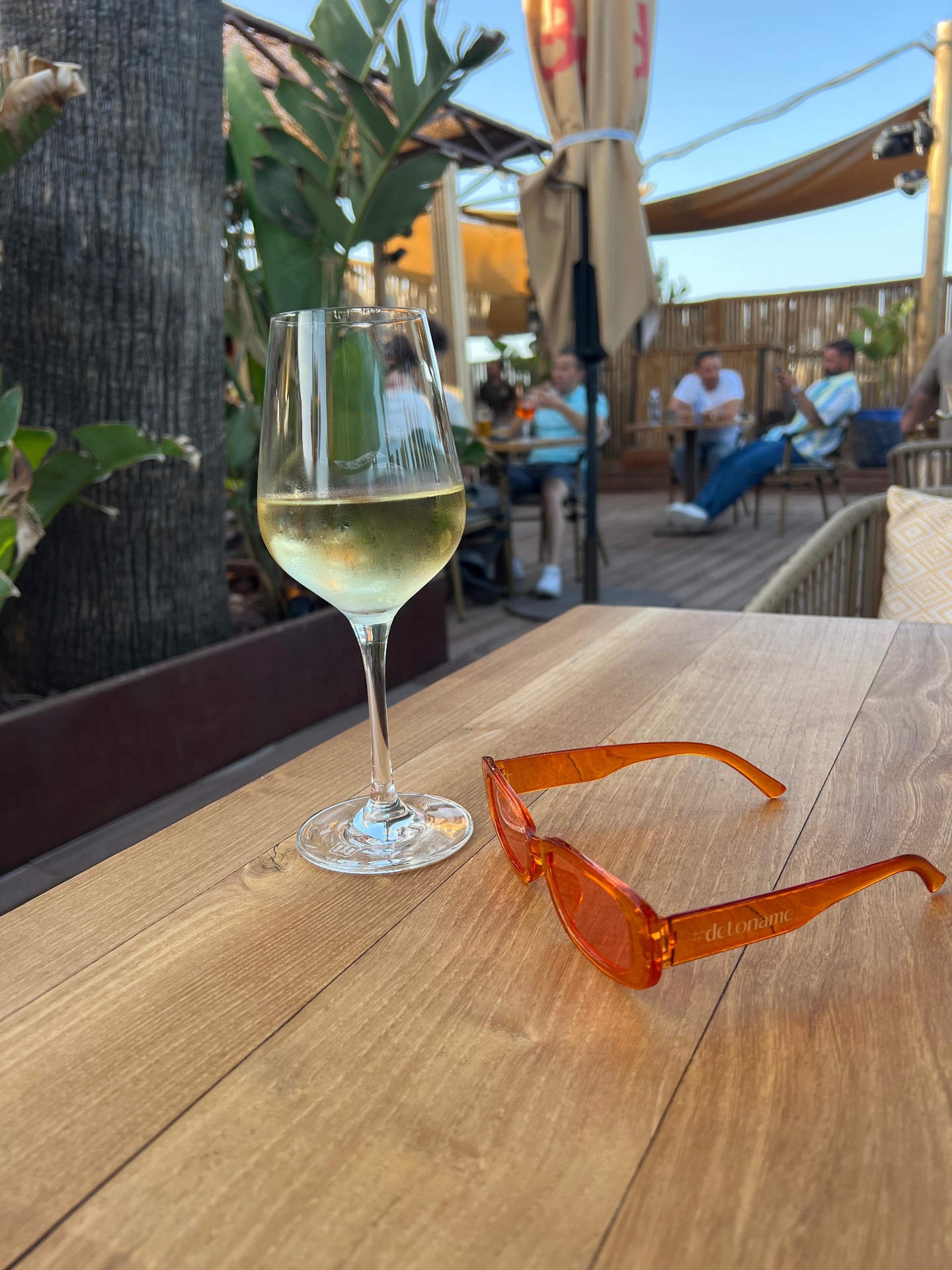 Gafas #detoname color naranja sobre mesa de chiringuito con copa de vino